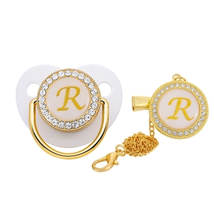 Detail of white and gold baby pacifier set with rhinestone letter R and matching clip chain