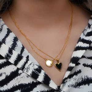 Gold layered necklace featuring white shell moon pendant and black heart charm on model