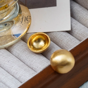 Macro view of matte golden spherical stud earrings with textured surface and needle back
