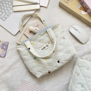 Top view detail of white quilted tote bag with colorful heart embroidery and tag