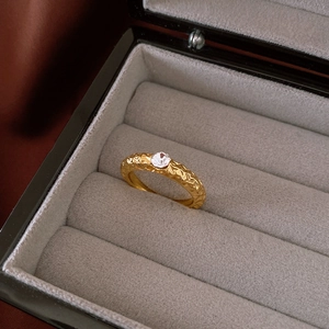 Detailed close-up of a gold-plated textured ring with a round zircon in a jewelry box