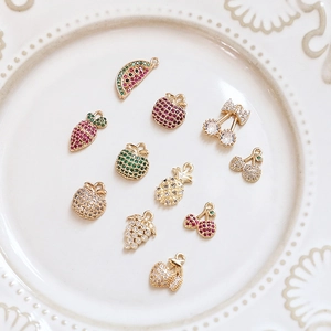 Detailed view of fruit-themed gold plated pendants with cubic zirconia on a ceramic plate