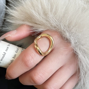 Detail of a minimalist gold wavy ring worn against white fur and newspaper background