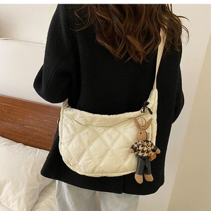 Quilted off-white crossbody bag with brown rabbit charm worn by model in home setting