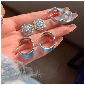 Detailed close-up of blue enamel stud and C-shaped earrings with silver and gold accents