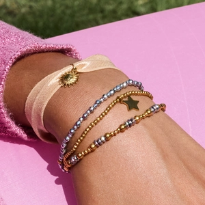 Layered gold bead bracelets with star and sun charms on a pink knit sweater cuff