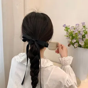 Rear view of a black satin bow hair clip with long ribbons on a braided hairstyle