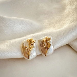 Close-up of golden floral earrings with baroque pearls on elegant beige silk fabric