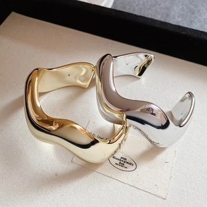 Vista dettagliata di bracciali aperti a onda in finiture metalliche oro e argento lucido