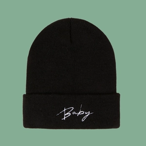 Close-up of black knitted beanie featuring white Baby script embroidery and ribbed texture