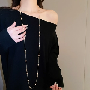 Détail d'un collier long en perles et chaîne dorée sur un pull en maille noire
