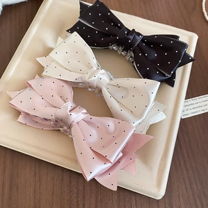 Close-up of three satin polka dot bow hair claws in black, cream, and pink colors