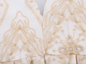 Detailed view of white cotton fabric featuring intricate gold floral embroidery and V-neckline