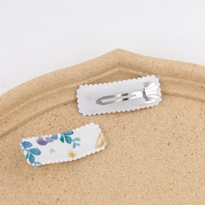 Detail of square snap hair clips with floral embroidery on white fabric texture