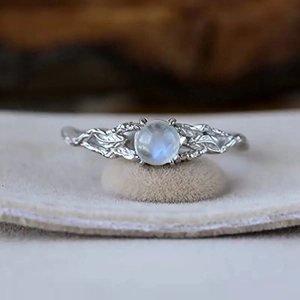 Silver moonstone ring with leaf vine engraving on a textured vintage wooden background