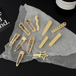 Flat lay of eleven assorted gold metallic hair clips on white paper and black background