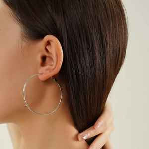 Close-up of a model wearing large polished silver titanium steel hoop earrings