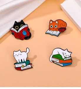 Macro shot of assorted cat and book enamel pins in black and orange on a peach background