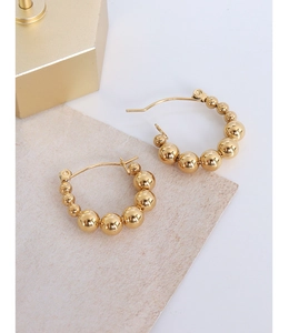 Detail showing polished gold-plated titanium steel beaded hoop earrings on textured paper
