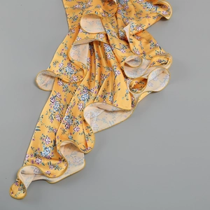 Detailed view of layered ruffles on a yellow floral satin dress with silk texture