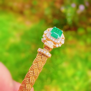 Macro shot of gold woven texture bangle with emerald green gemstone and pave diamonds