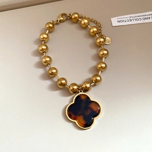 Detail of beaded stainless steel bracelet with clover pendant and tortoiseshell texture