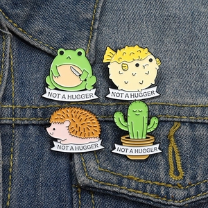 Cute cartoon animal enamel pins featuring frog, hedgehog, and cactus with Not a Hugger text