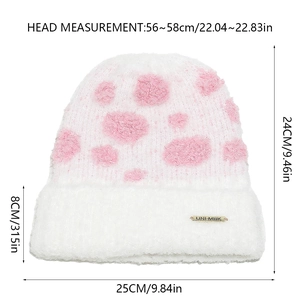 Detailed close-up of a white plush knit hat with pink dots and gold logo plaque