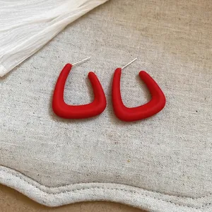 Minimalist geometric acrylic stud earrings in matte wine red finish on linen background