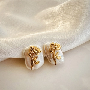 Close-up of golden flower earrings with irregular baroque pearls on white silk fabric