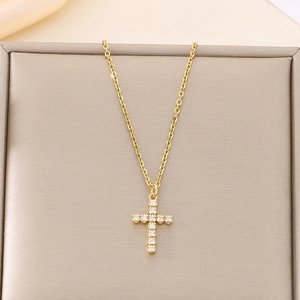 Close-up of gold cross pendant with pavé crystals hanging on a champagne display stand