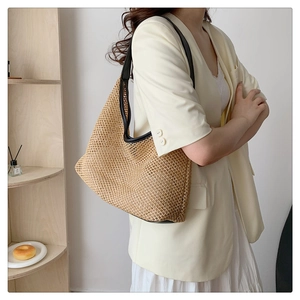 Detail of woven straw tote bag with black leather straps on a minimalist indoor shelf