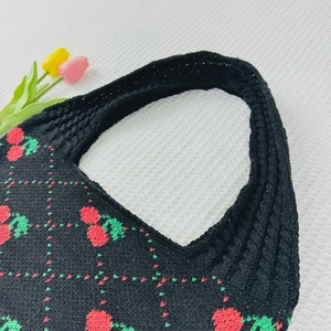 Close-up of black knitted tote bag featuring red strawberry patterns and green leaves