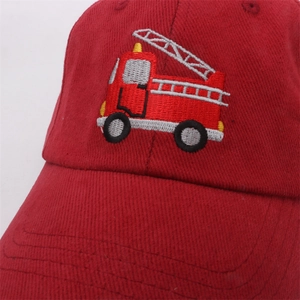 Close-up of red kids baseball cap featuring detailed fire truck embroidery on cotton fabric