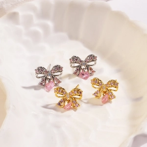 Detailed close-up of gold and silver bow earrings with pink teardrop crystals in a shell dish