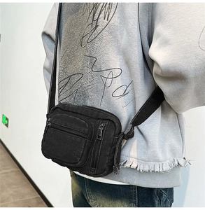 Detail of black washed denim crossbody bag showing multi-zipper pockets and adjustable strap