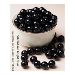 Close-up of highly polished black agate beads with a smooth mirror finish in a ceramic bowl