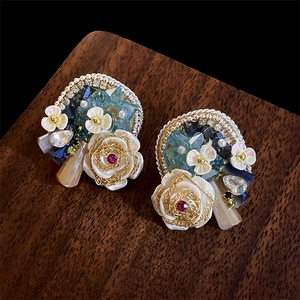 Detail of handmade flower earrings with white roses, blue crystals and golden wires