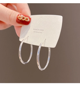 Macro shot of large 925 silver post hoop earrings held against a neutral brown backdrop