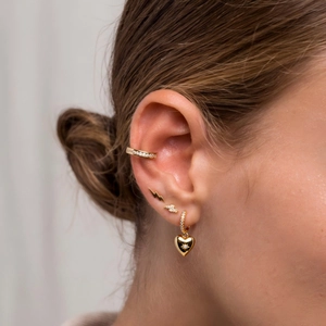Gold heart and lightning bolt earrings set with zircon stones on a model ear