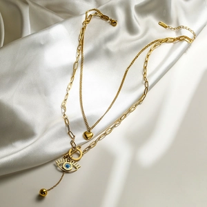 Double-layer gold Evil Eye necklace with heart pendant on soft white silk fabric