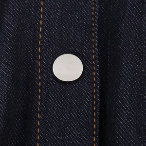 Vista macro del denim scuro con bottone in metallo argento e cuciture a contrasto