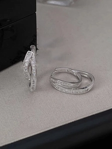 Detail of silver double hoop earrings with baguette-cut cubic zirconia on a gray background