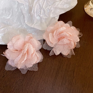 Detail of pink fabric flower earrings with layered petals on a rustic wooden surface