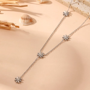 Silver Y-shaped stainless steel necklace with small flower pendants on a beach theme backdrop
