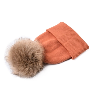Detailed ribbed knit texture of orange baby winter hat with large faux fur pompom decor