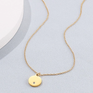 Detailed view of a gold circular pendant necklace with a small diamond on a fine chain