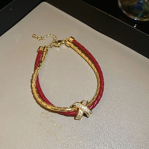 Détail d'un bracelet en cuir tressé rouge avec des accents croisés dorés en zircon