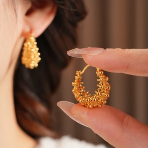 Gros plan sur des boucles d'oreilles dorées avec grappes de perles et sphères en métal