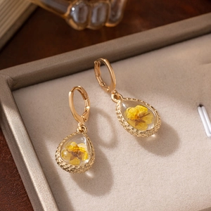 Macro view of gold waterdrop earrings featuring real yellow dried flowers in glass